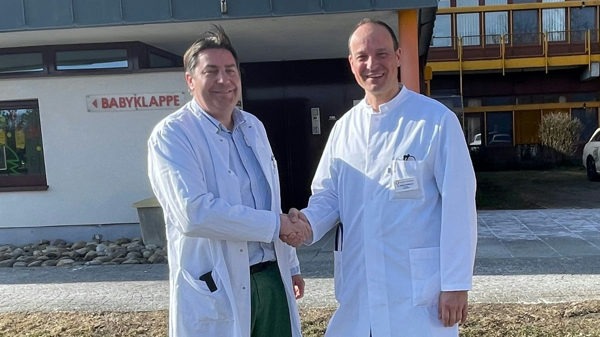 Zwei Ärzte schütteln sich vor einem Krankenhaus die Hände.