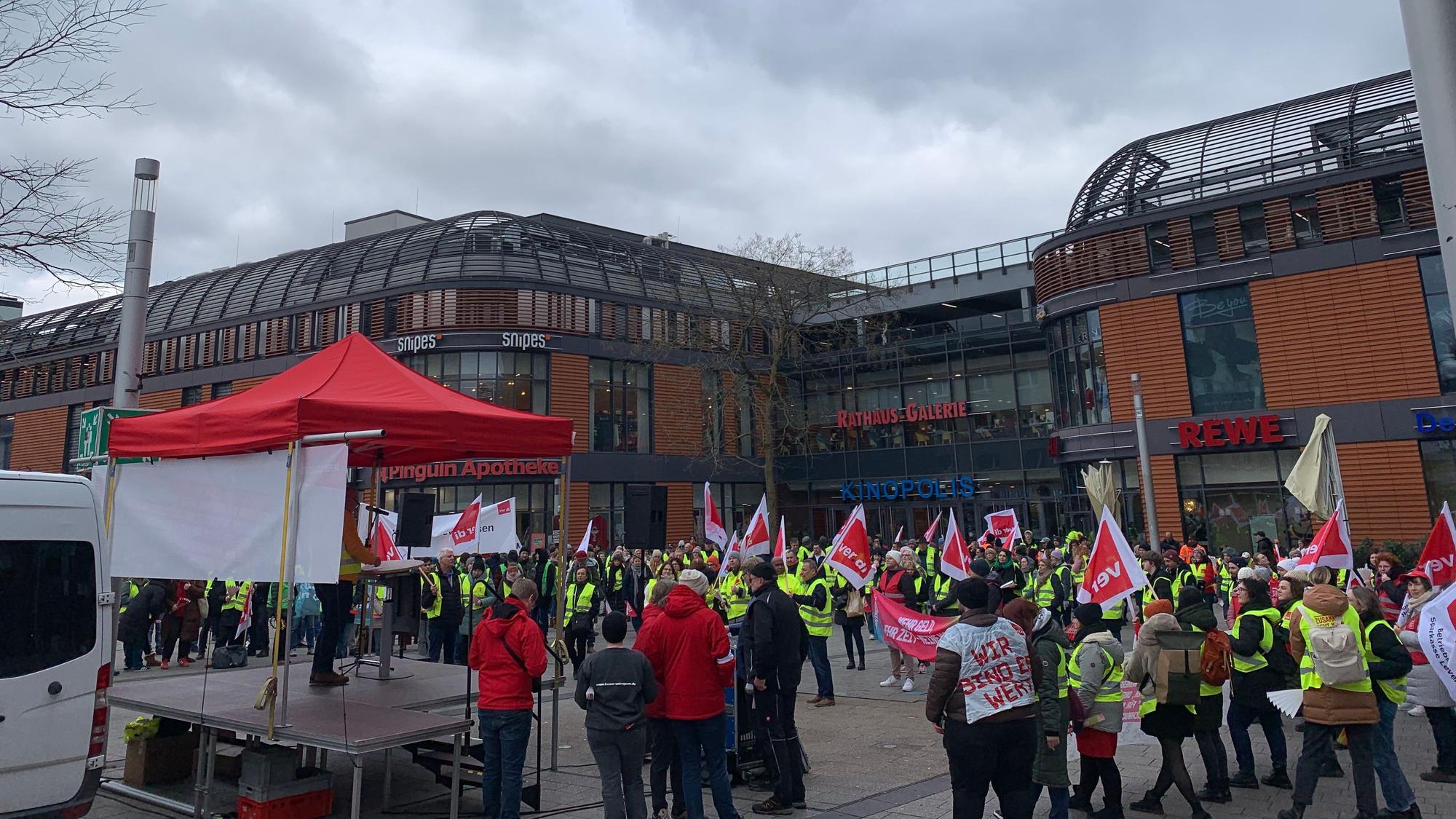 Viele Menschen stehen mit Fahnen und Warnwesten auf einem Platz.