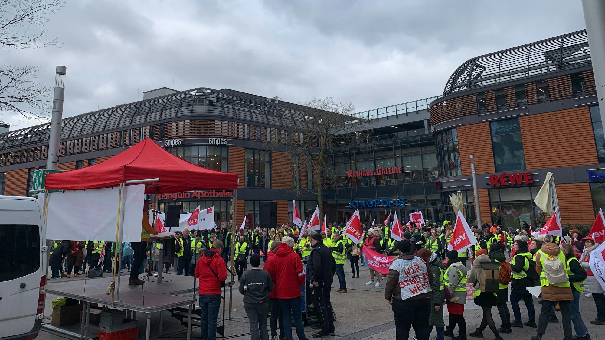 Viele Menschen stehen mit Fahnen und Warnwesten auf einem Platz.