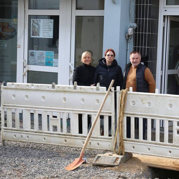 Drei Menschen hinter Speerbaken einer Baustelle, die nur wenig Platz zu den Ladenlokalen lassen.