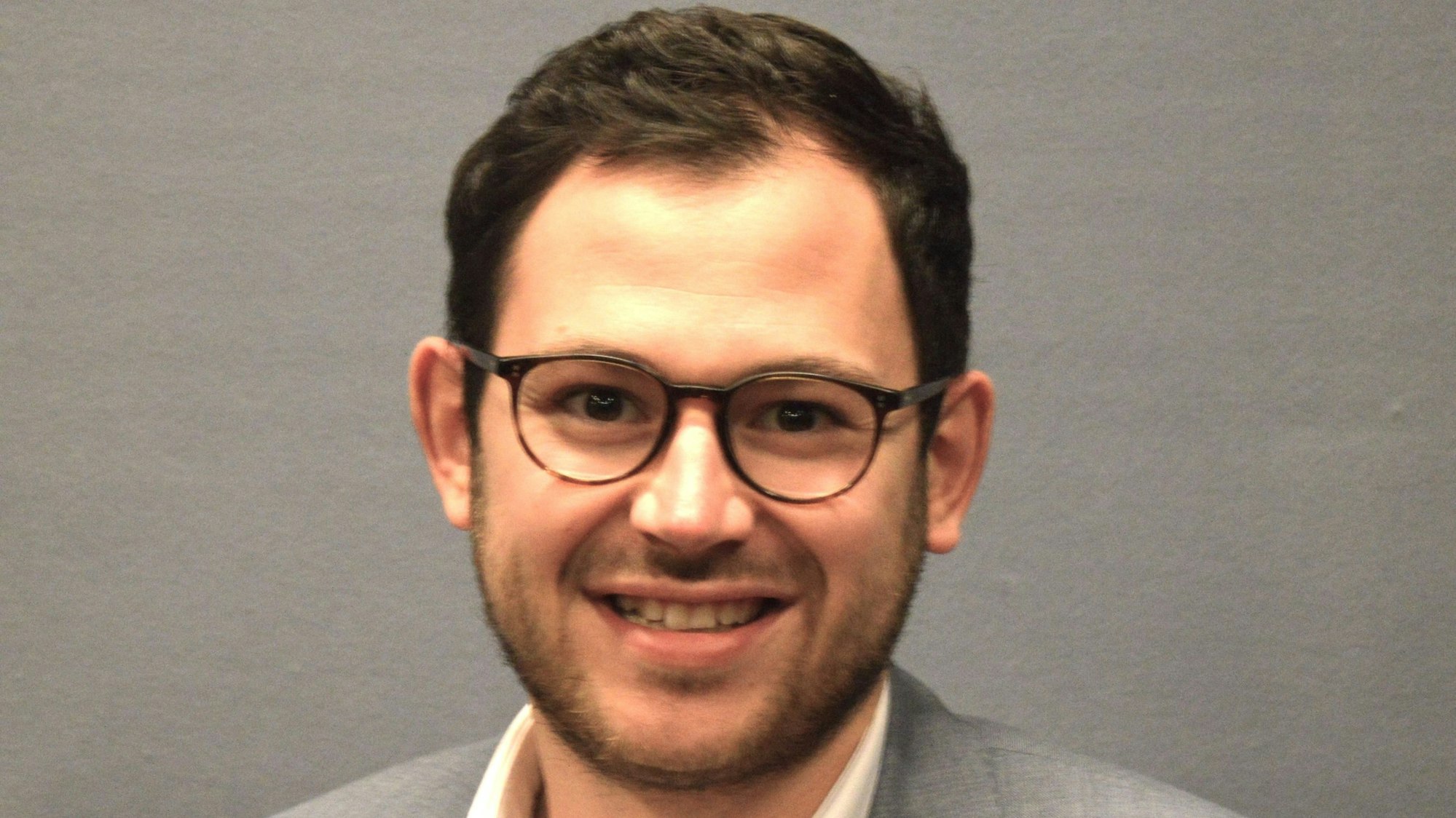 Porträtfoto von Emmanuel Kunz. Er trägt einen grauen Anzug und Brille.