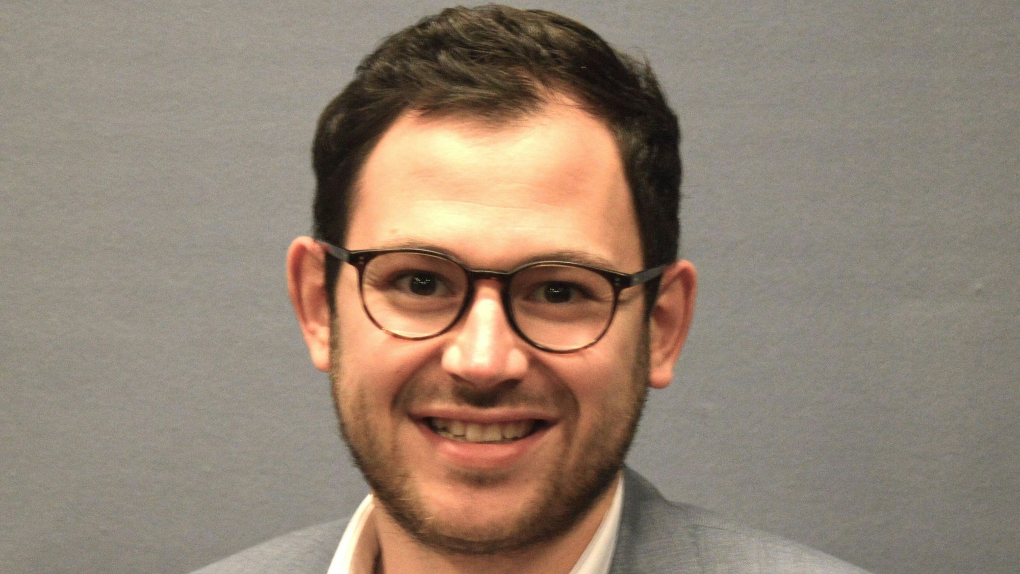 Porträtfoto von Emmanuel Kunz. Er trägt einen grauen Anzug und Brille.