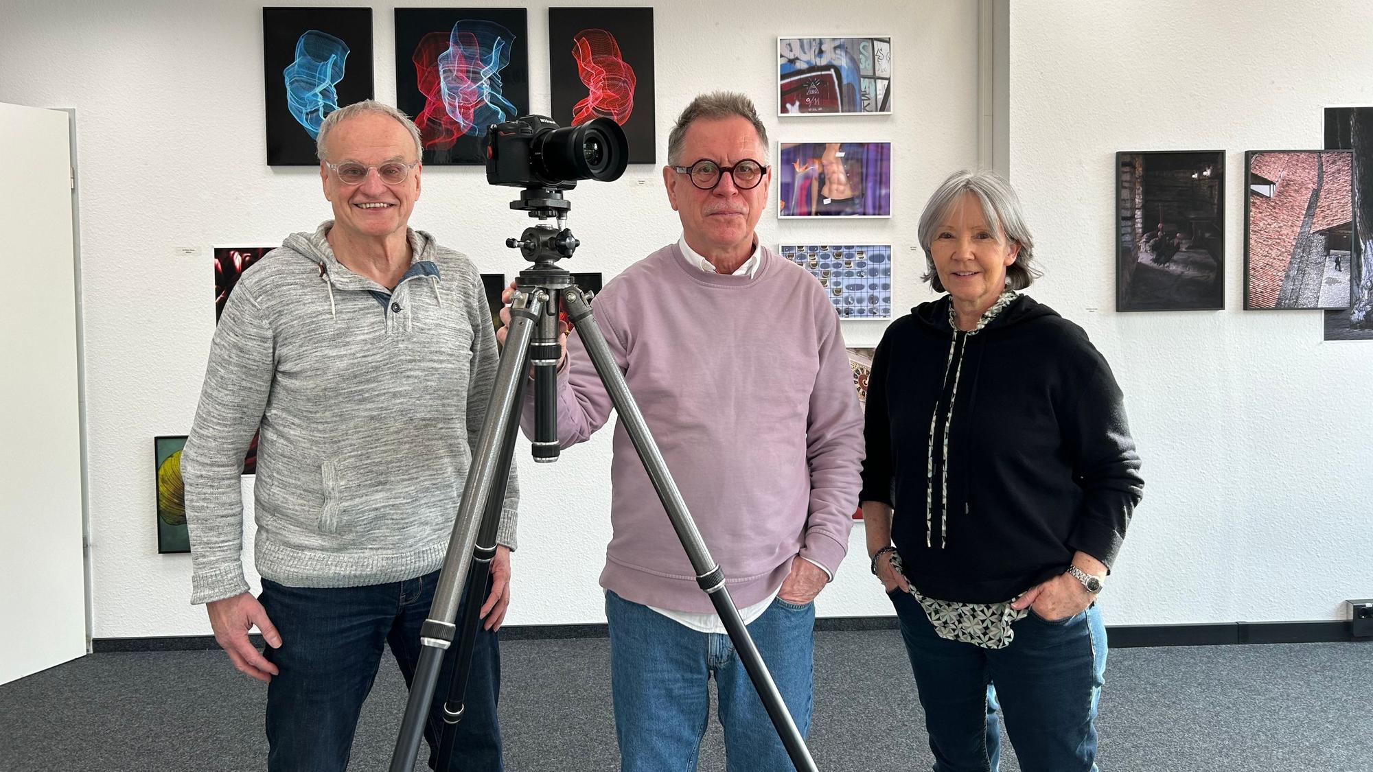 Drei Menschen stehen an einer Kamera in einer Fotoausstellung.