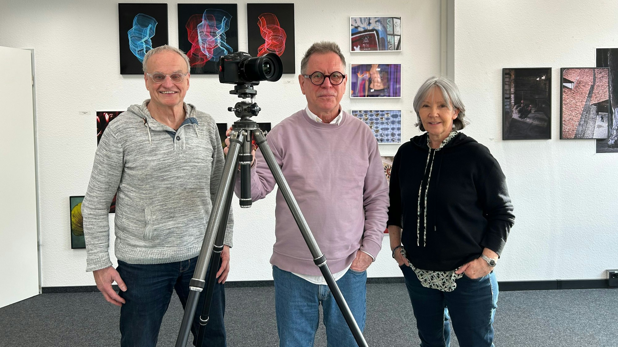 Drei Menschen stehen an einer Kamera in einer Fotoausstellung.