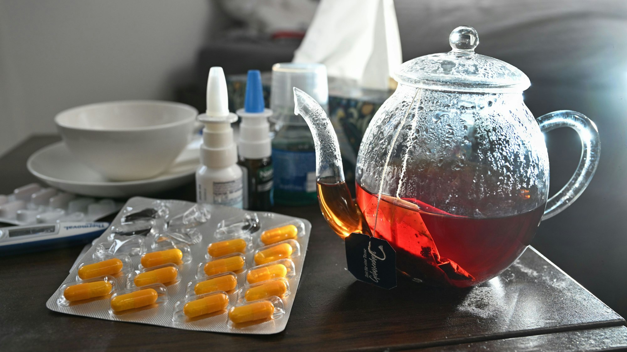 Medikamente und eine Kanne und Tasse Tee zur Bekämpfung einer Erkältung sind auf einem Nachttisch aufgestellt. (Symbolbild)
