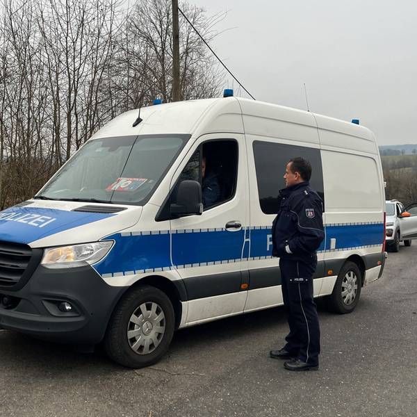 Ein Einsatzfahrzeug der Polizei steht auf einer Straße, ein Polizist steht daneben.