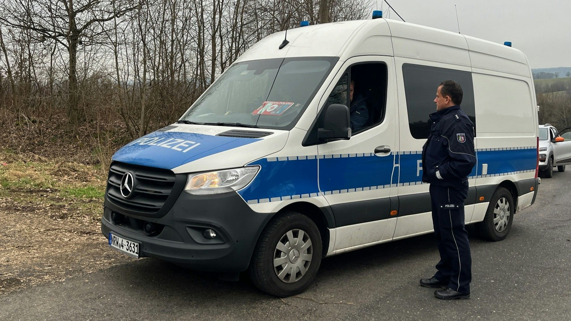 Ein Einsatzfahrzeug der Polizei steht auf einer Straße, ein Polizist steht daneben.