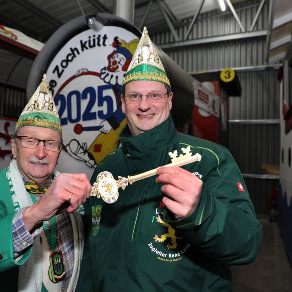 Helmut Kraus und sein Nachfolger als Zugleiter, René Karla, stehen mit einem großen Schlüssel vor der Zugleiter-Lokomotive des Bergisch Gladbacher Karnevalszugs.