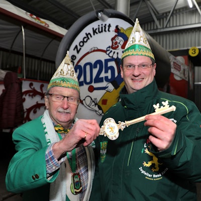 Helmut Kraus und sein Nachfolger als Zugleiter, René Karla, stehen mit einem großen Schlüssel vor der Zugleiter-Lokomotive des Bergisch Gladbacher Karnevalszugs.