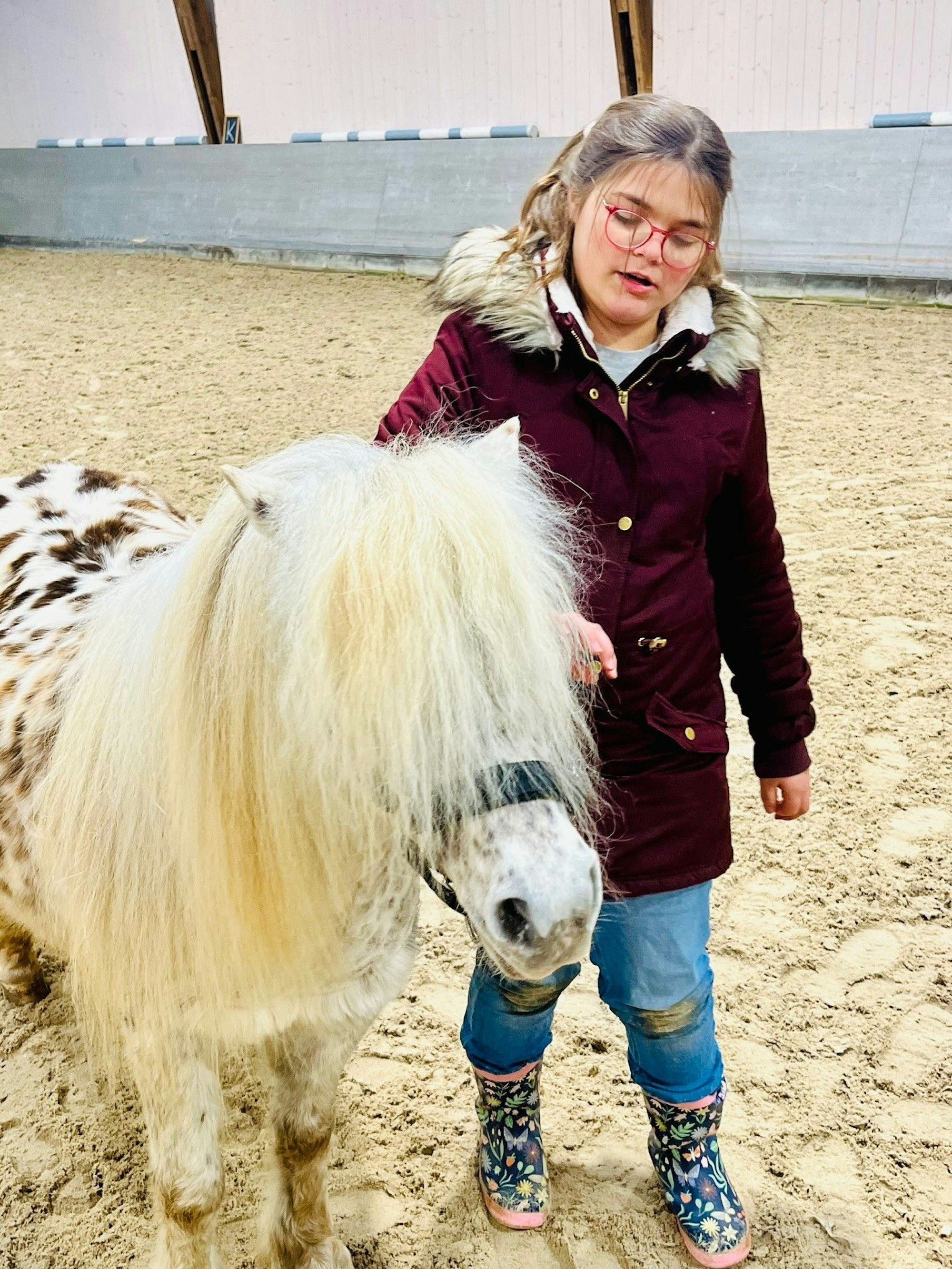 Ein Mädchen steht im Reitstall mit einem weißen Shetlandpony mit schwarzen Flecken.