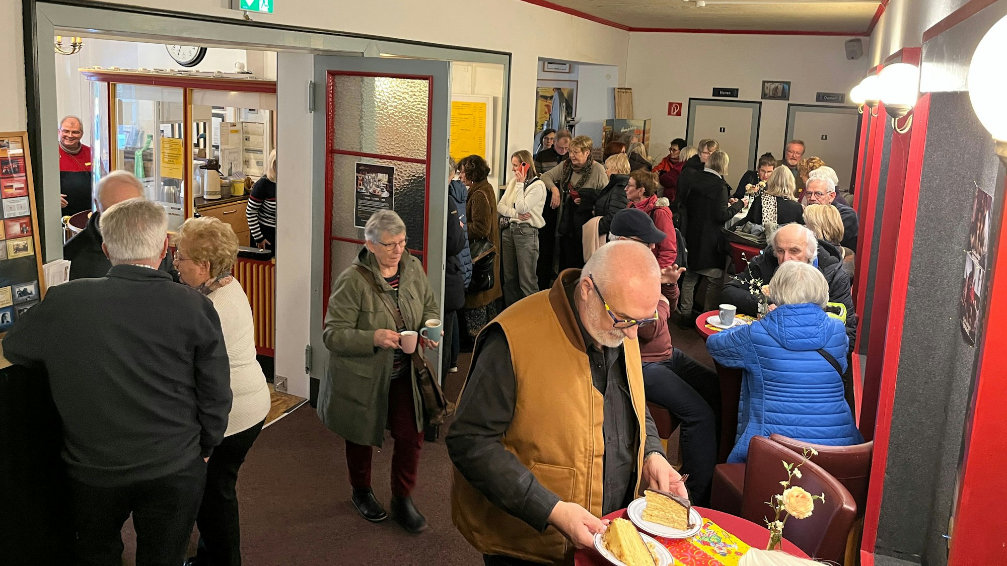 Im Foyer eines Kinos sitzen und stehen viele Menschen bei Kaffee und Kuchen zusammen.