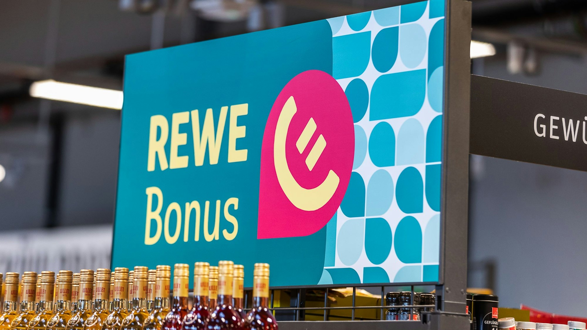 Ein Werbeschild für Rewe-Bonus steht in einem Supermarkt.