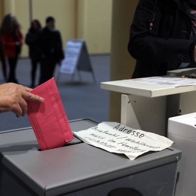 Eine Person wirft einen Stimmzettel in eine Wahlurne.