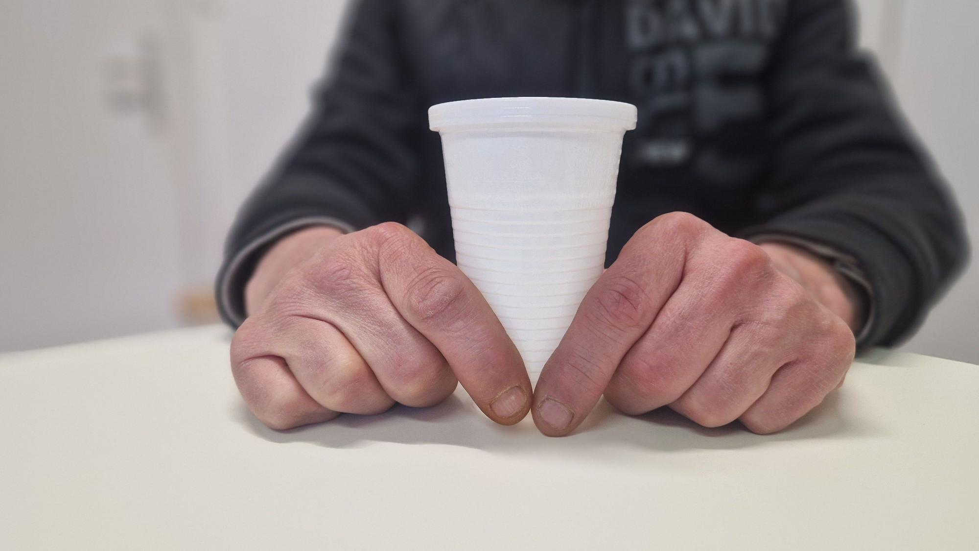 Nahaufnahme: Zwei Hände halten einen Plastikbecher.