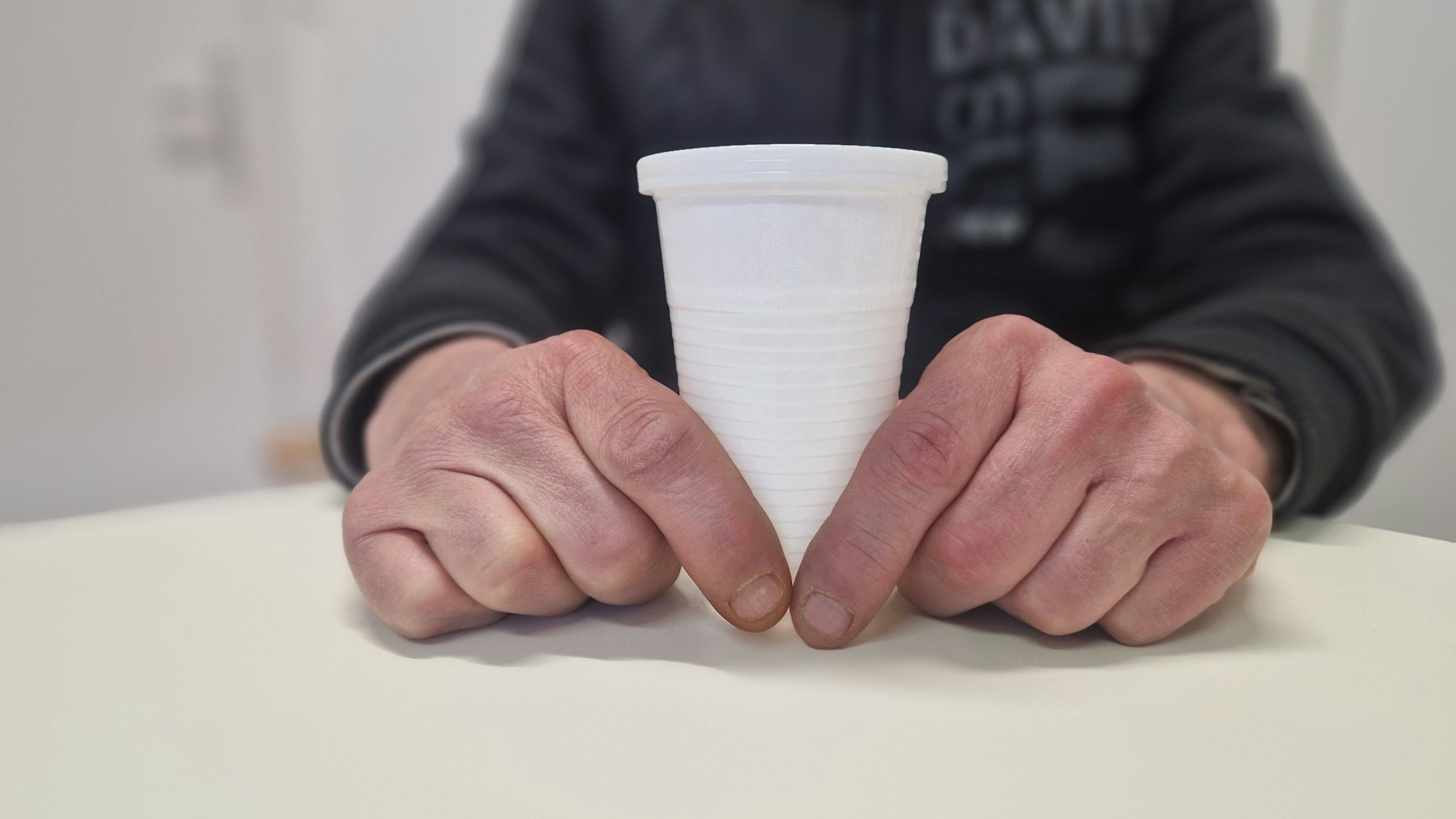 Nahaufnahme: Zwei Hände halten einen Plastikbecher.