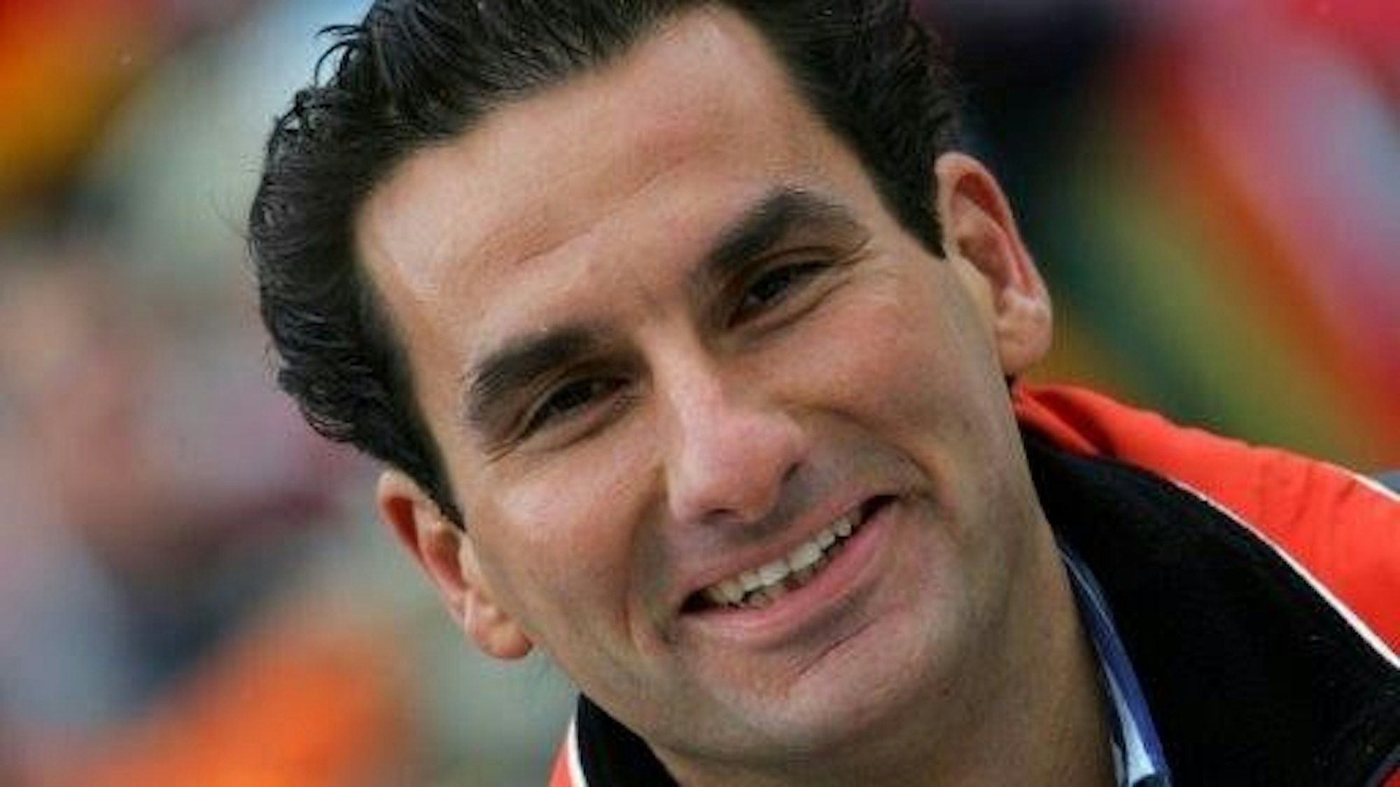 Auf dem Bild ist ein lächelnder Mann mit dunklem Haar zu sehen.