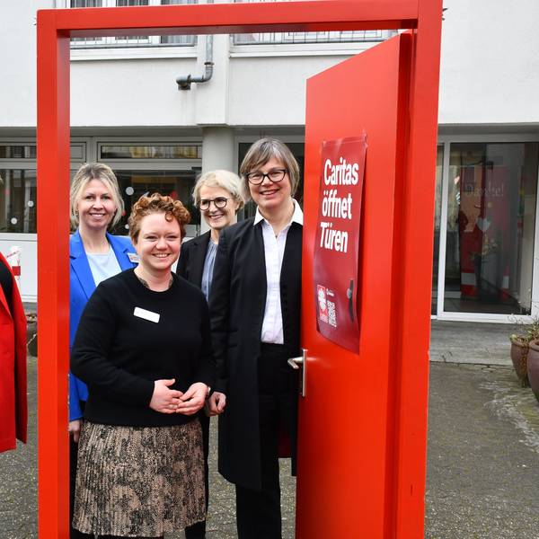 Das Foto zeigt das Führungsteam der Caritas vor einer geöffneten symbolischen roiten Tür.