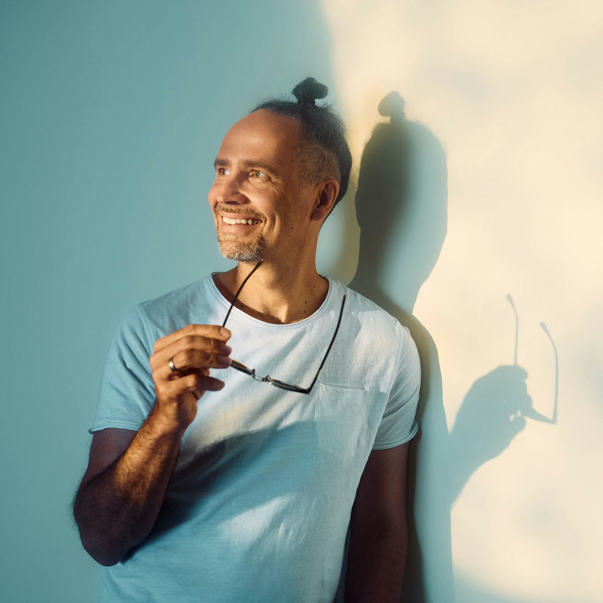 Ein Mann hält eine Sonnenbrille in der Hand und lehnt an einer Wand.