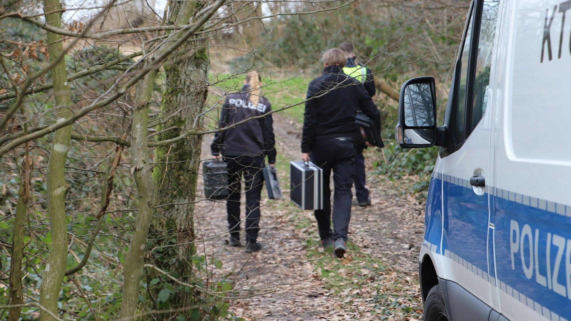 Eine Frau und ein Mann mit Koffern in der Hand gehen auf ein Waldgrundstück.