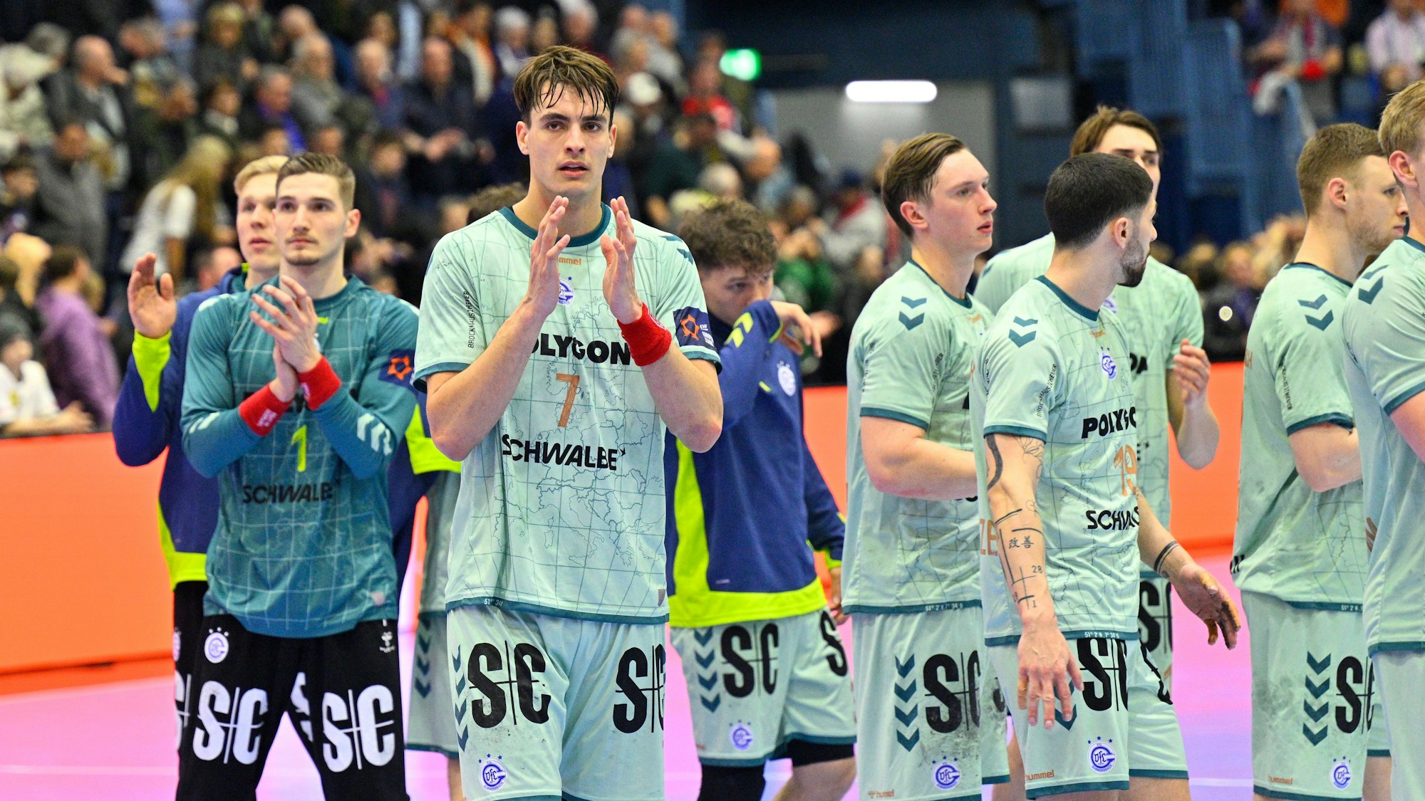 Mehrere Handballer des VfL Gummersbach applaudieren nach einem Spiel gegen Flensburg in Richtung der Fans auf den Tribünen.