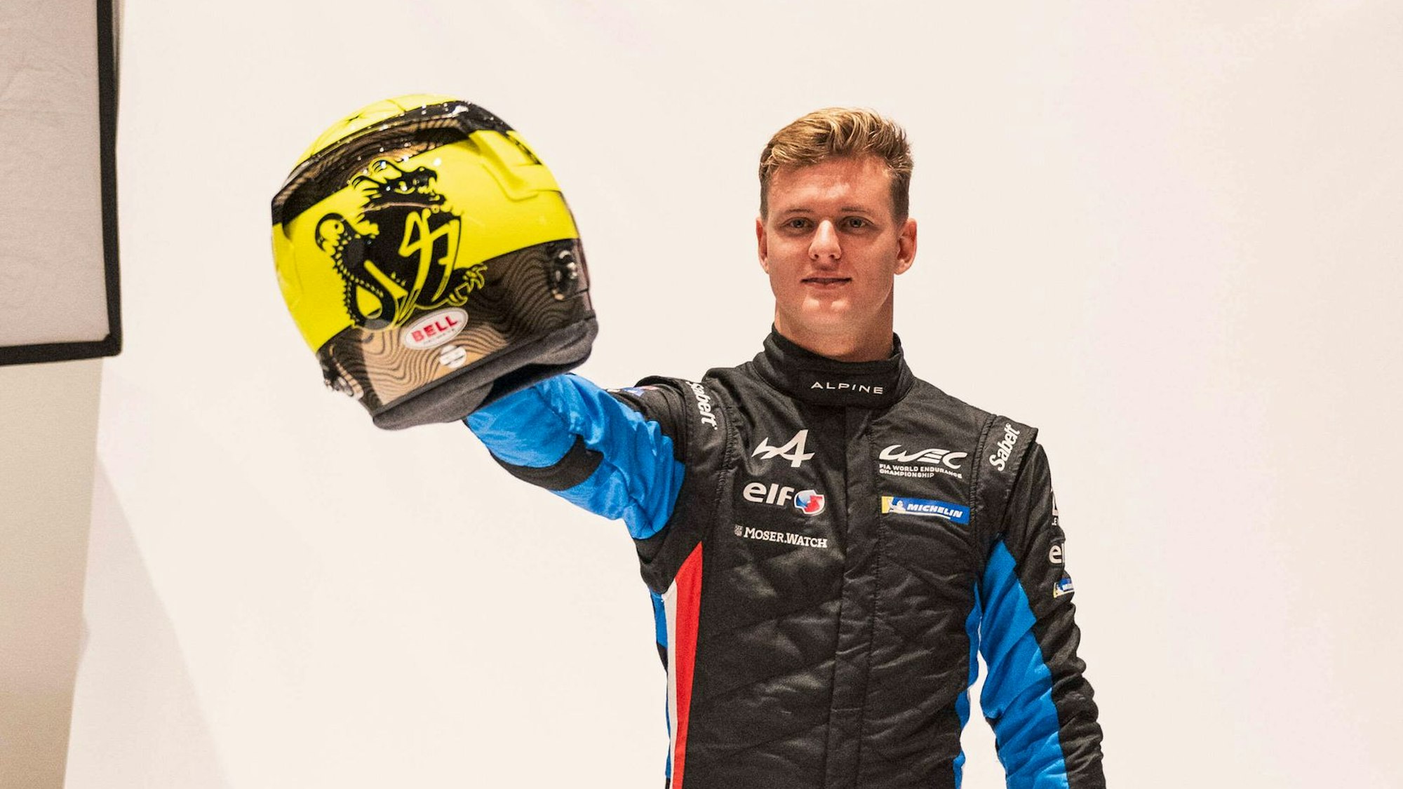 Mick Schumacher hält einen gelben Rennsporthelm in die Kamera.