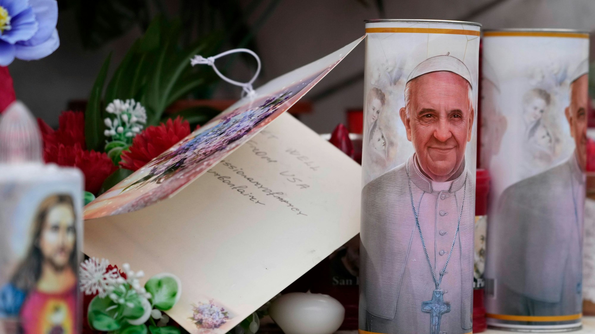 Kerzen mit dem Bild von Papst Franziskus werden unter der Statue des verstorbenen Papstes Johannes Paul II. vor der Poliklinik Agostino Gemelli in Rom niedergelegt, wo der Papst seit Freitag, 14. Februar 2025, behandelt wird.