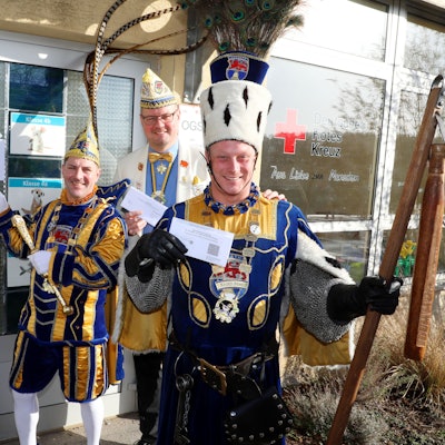 Jungfrau Timona (Timo Boxberg), Prinz Andreas I. (Lüdenbach), Prinzenführer Niklas Habers und Bauer René (Doppstadt) vom Overather Dreigestirn stehen vor einem Wahllokal in der Grundschule von Vilkerath.