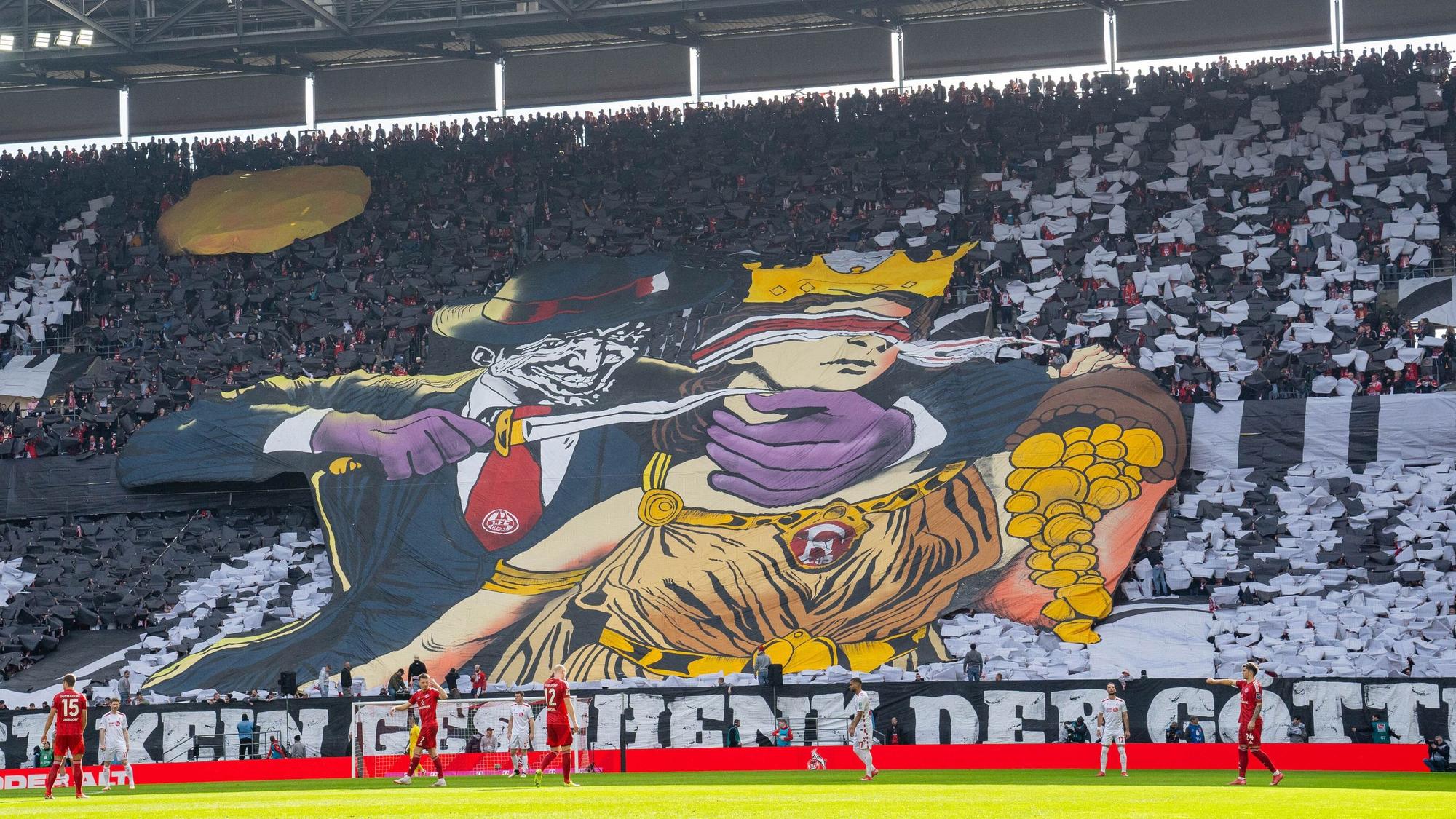 Ein Transparent, das Kölner Fans im Rhein-Energie-Stadion entfalteten, zeigt eine Comic-Figur, die einer Frau mit verbundenen Augen ein Messer an den Hals hält. Die Frau ist der Göttin Fortuna nachempfunden und schüttet Gold aus einem Füllhorn.