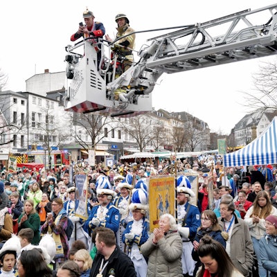Jecke unter dem Korb einer Drehleiter auf einem Marktplatz.