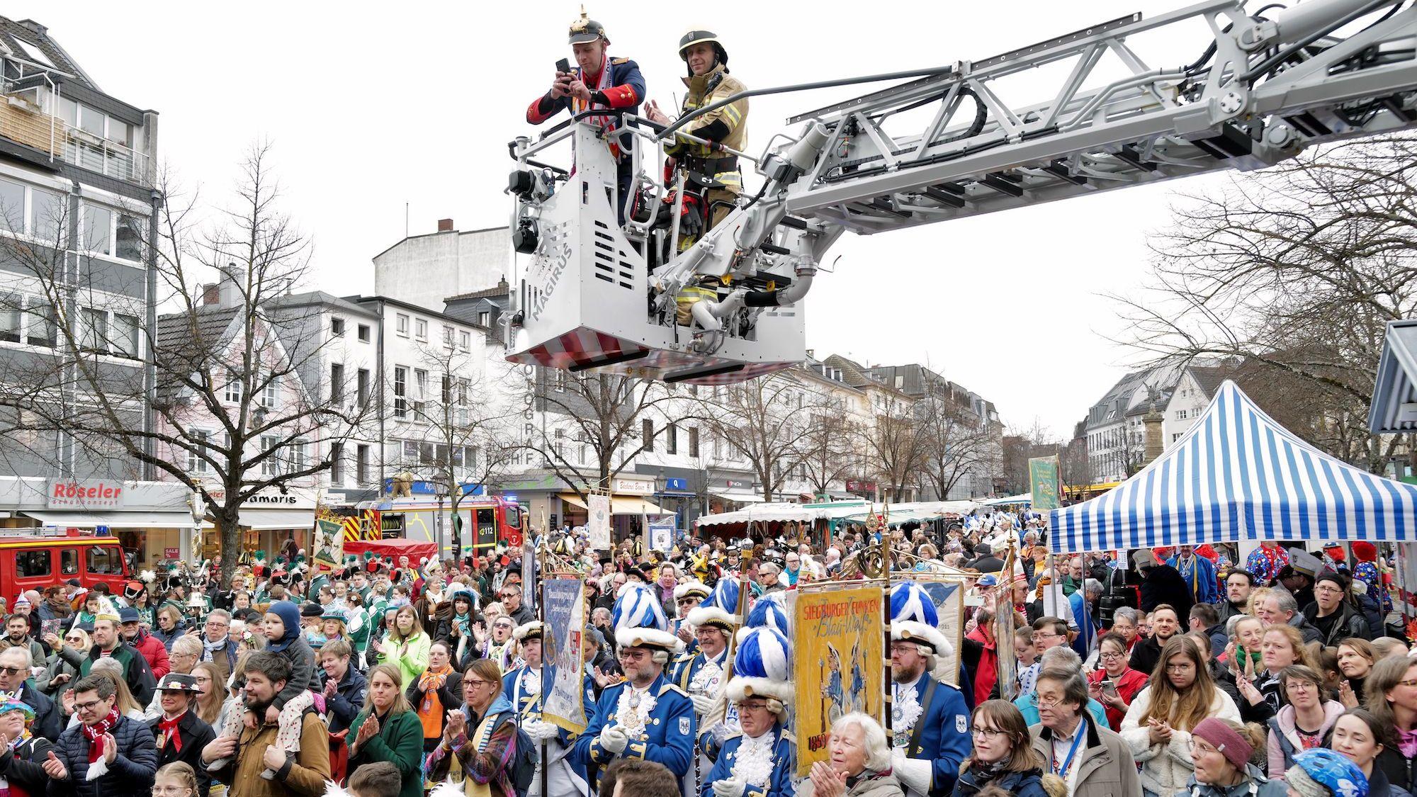 Jecke unter dem Korb einer Drehleiter auf einem Marktplatz.