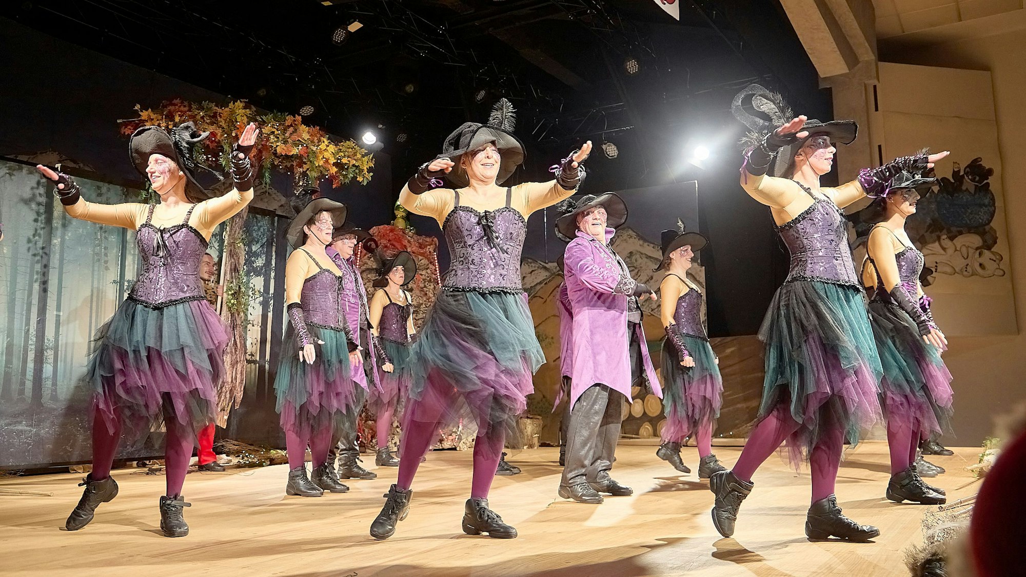 Als Hexen verkleidete Tänzerinnen tanzen auf der Bühne um einen Mann im Zaubererkostüm, der in ihrer Mitte steht.