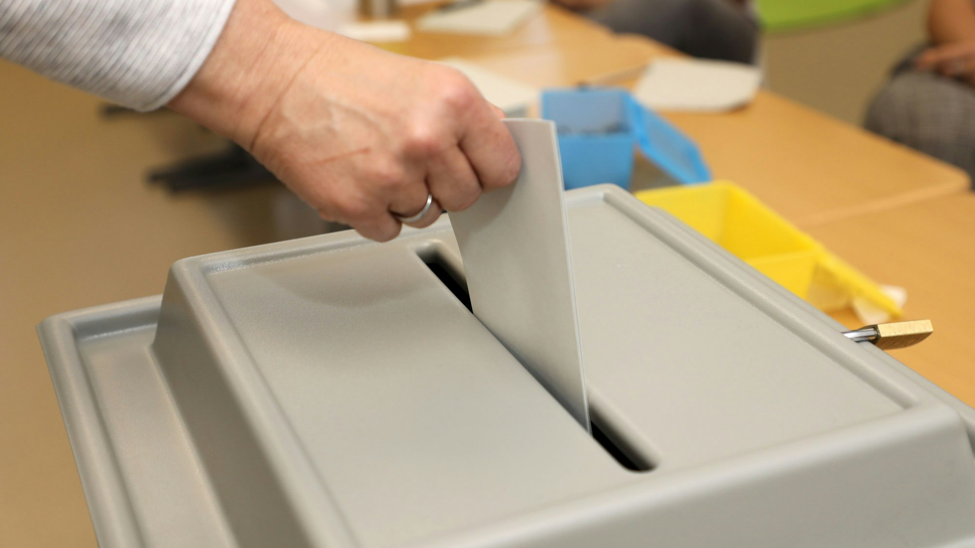 Das Foto zeigt einen Wahlzettel, den ein Wähler in eine Wahlurne gibt