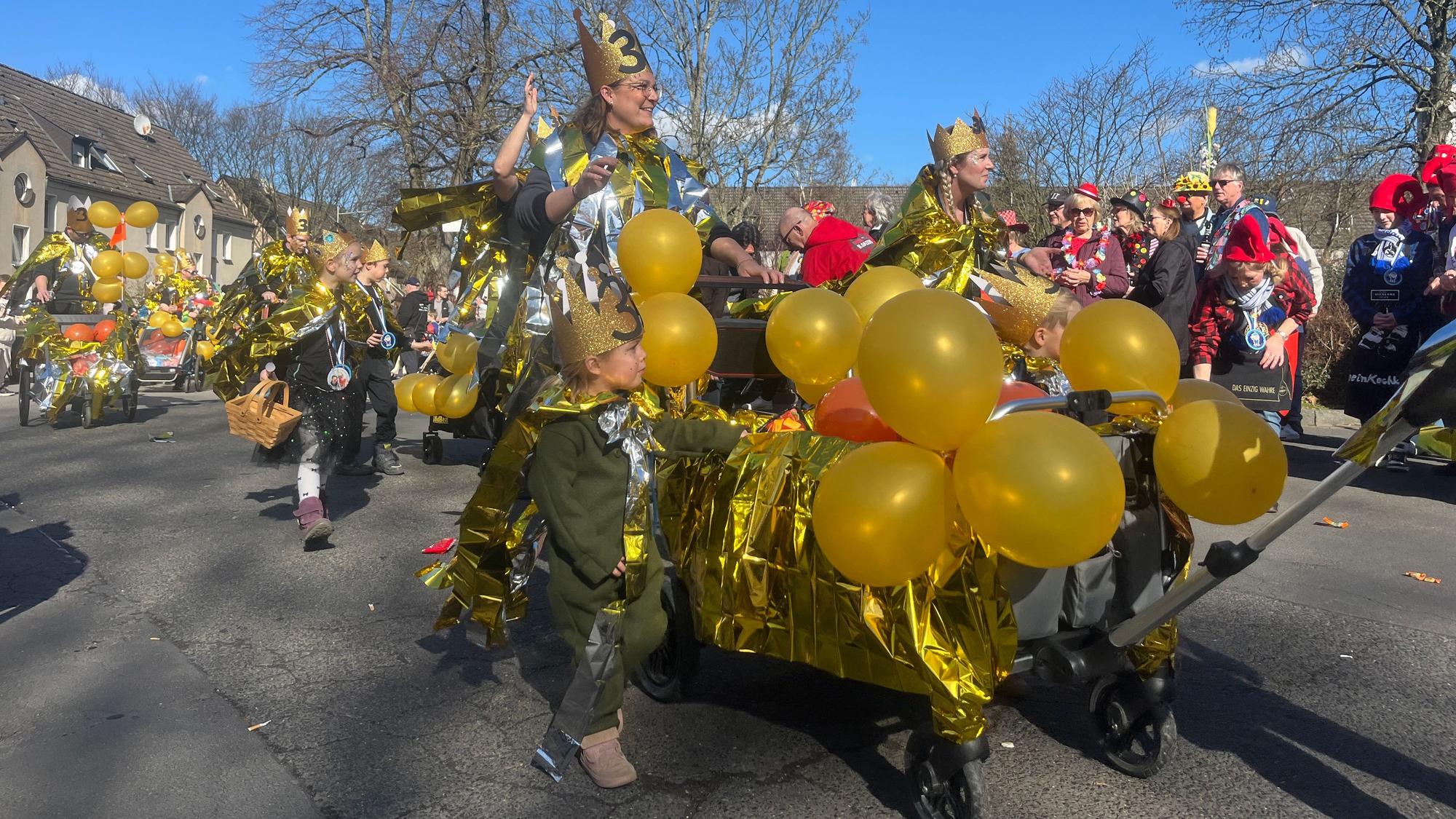 Mit gold und silbern glänzenden Kostümen ziehen Eltern und ihre Kinder im Zug mit.