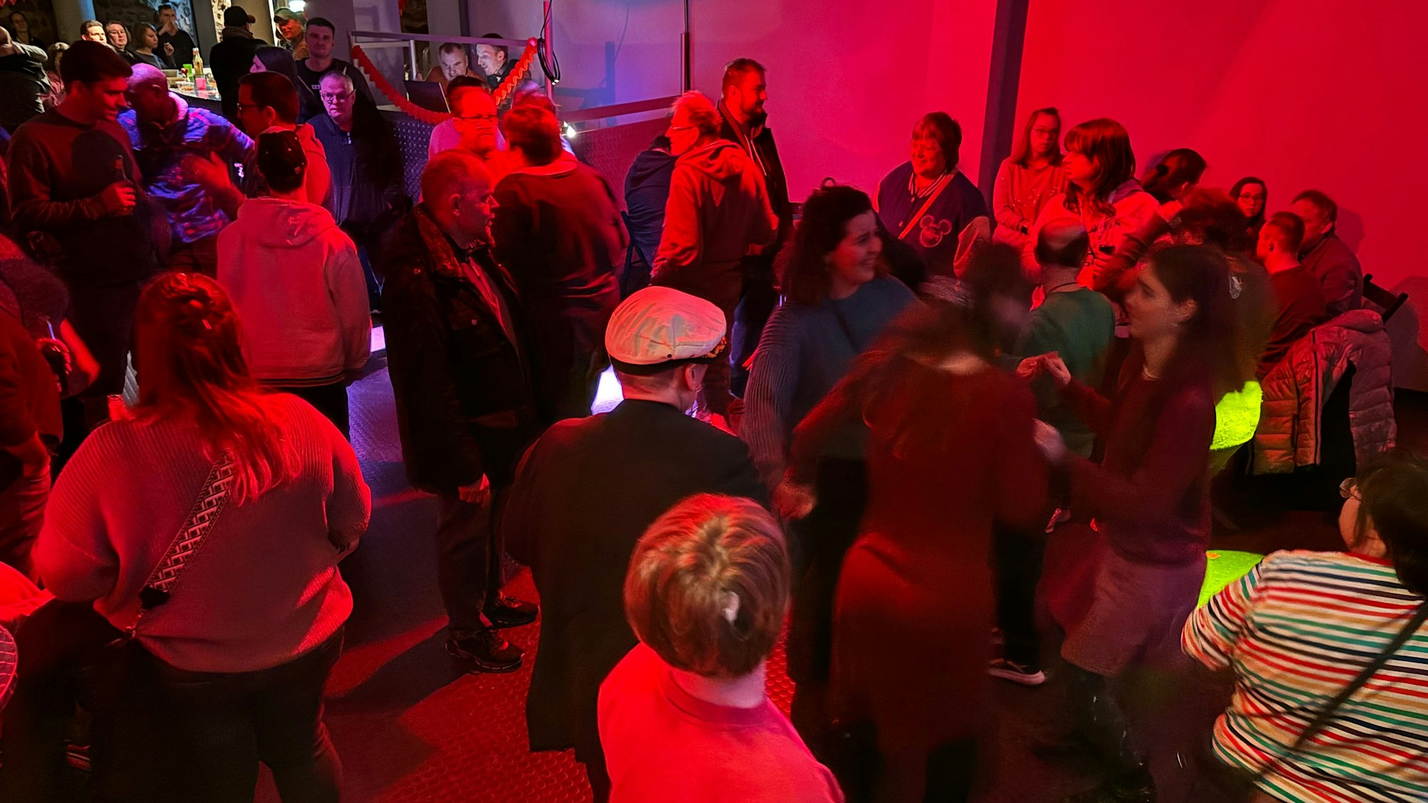 Mehrere Menschen tanzen in einem Raum, der mit einem roten Licht beleuchtet wird.