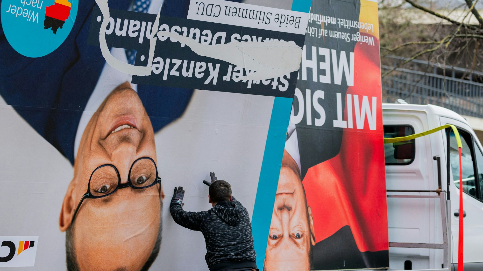 Arbeiter laden ein Wahlplakat, das den Vorsitzenden der CDU, Merz, zeigt, auf einen Lieferwagen neben einem Plakat, das Bundeskanzler Scholz (SPD) zeigt.