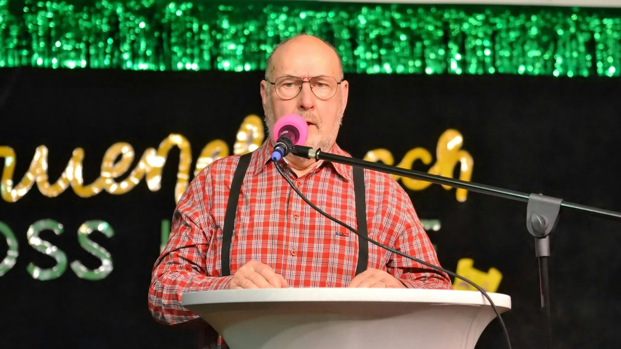 Auf der geschmückten Karnevalsbühne steht ein Redner am Mikrofon.