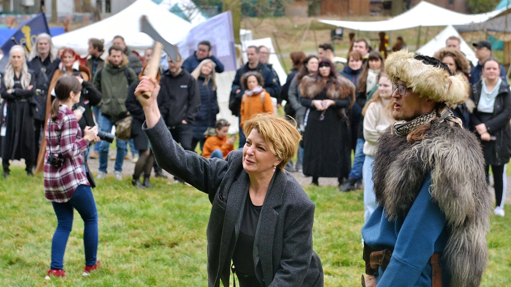 Die Schauspielerin Jördis Triebel hält eine Axt in der rechten Hand und nimmt Schwung, um sie beim Axtwurfwettbewerb auf dem Gelände der Burg Satzvey möglichst weit zu werfen.