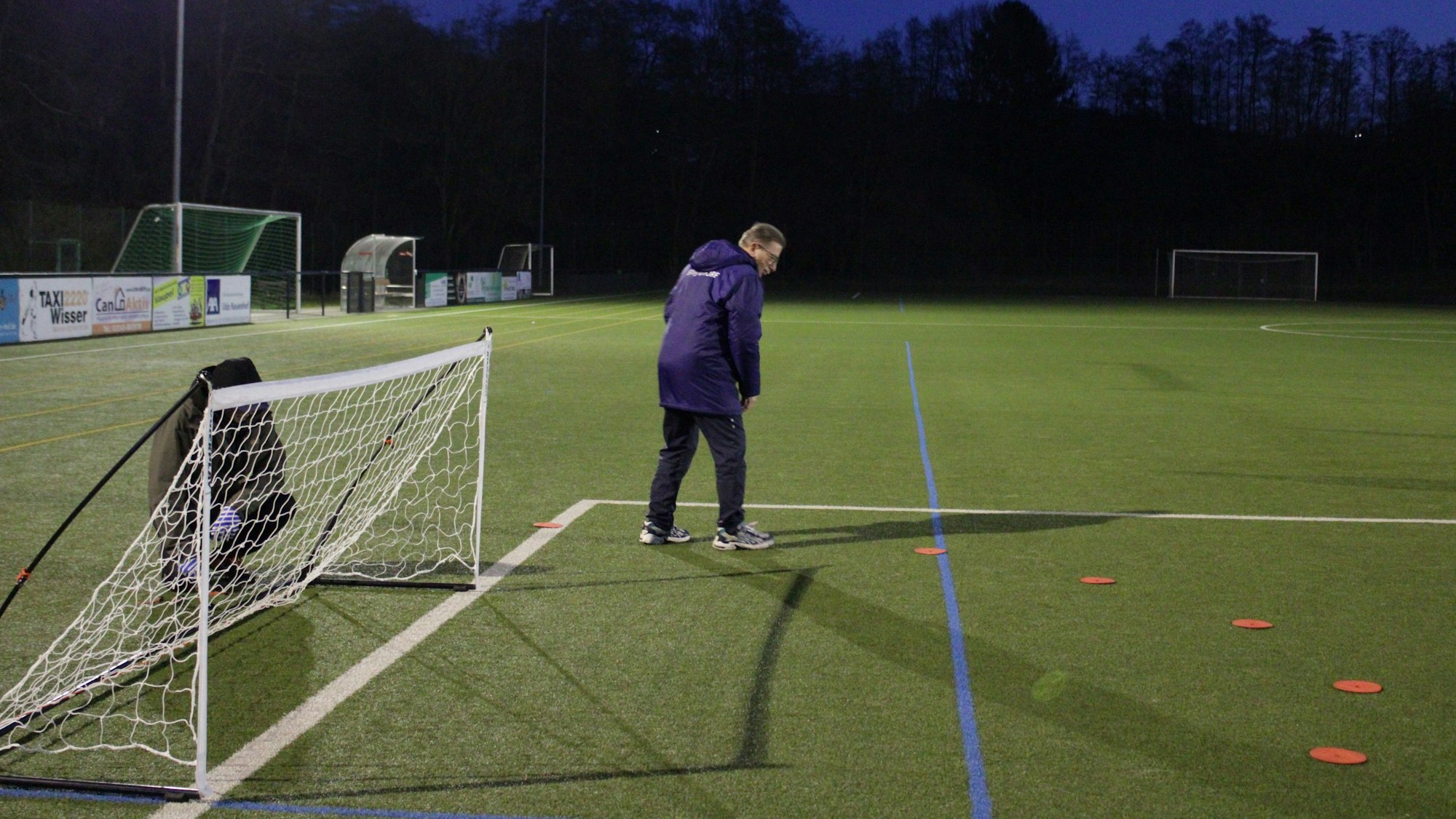 Ein Mann steht auf einem Fußballfeld und legt orange Markierungen um ein Tor herum.