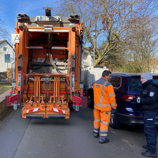 Ein Müllauto steht auf einer Straße zwischen einer Grundstücksmauer und geparkten Fahrzeugen ist kaum ein Durchkommen.