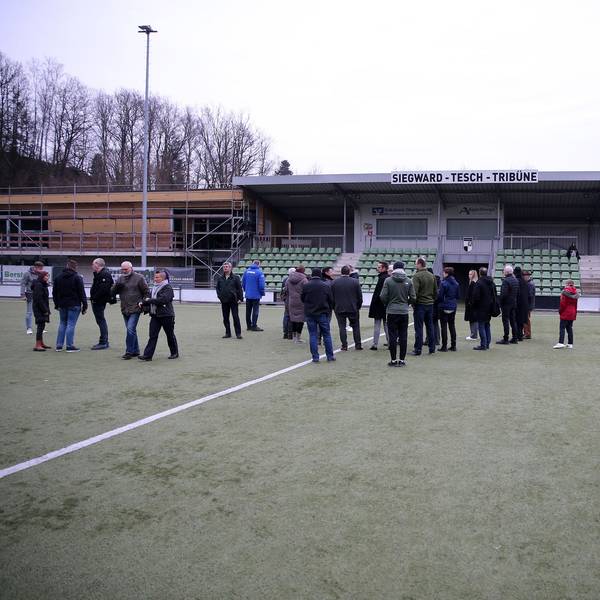 Eine Gruppe steht auf dem Rasen einer Sportanlage.