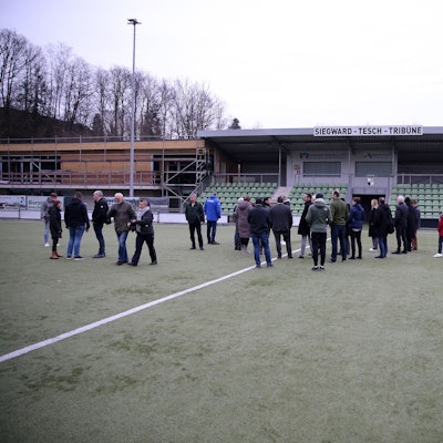 Eine Gruppe steht auf dem Rasen einer Sportanlage.