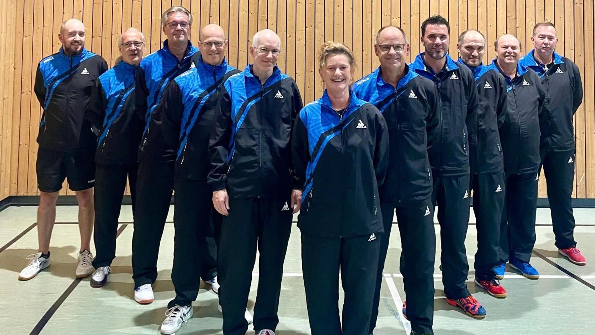 Die Mitglieder der Tischtennismannschaft des SV Kirchheim stehen in blau-schwarzen Trainingsanzügen in Form eines V in einer Sporthalle.