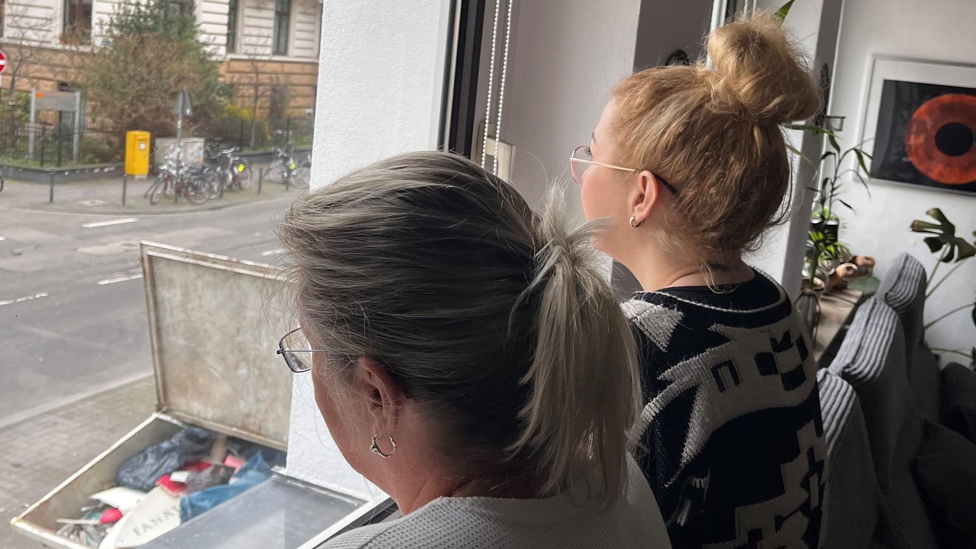 Frauen blicken aus ihrem Wohnungsfenster auf Müll.