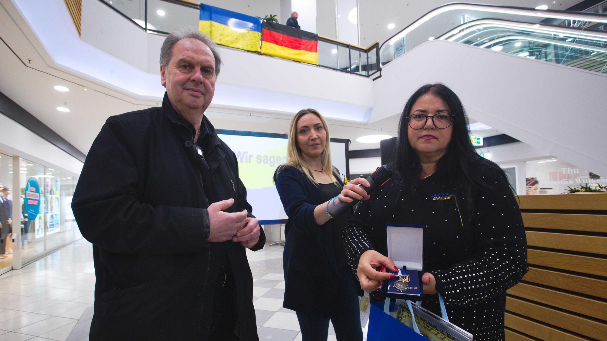 Ein Mann erhält von zwei Frauen eine Urkunde und einen ukrainischen Orden.