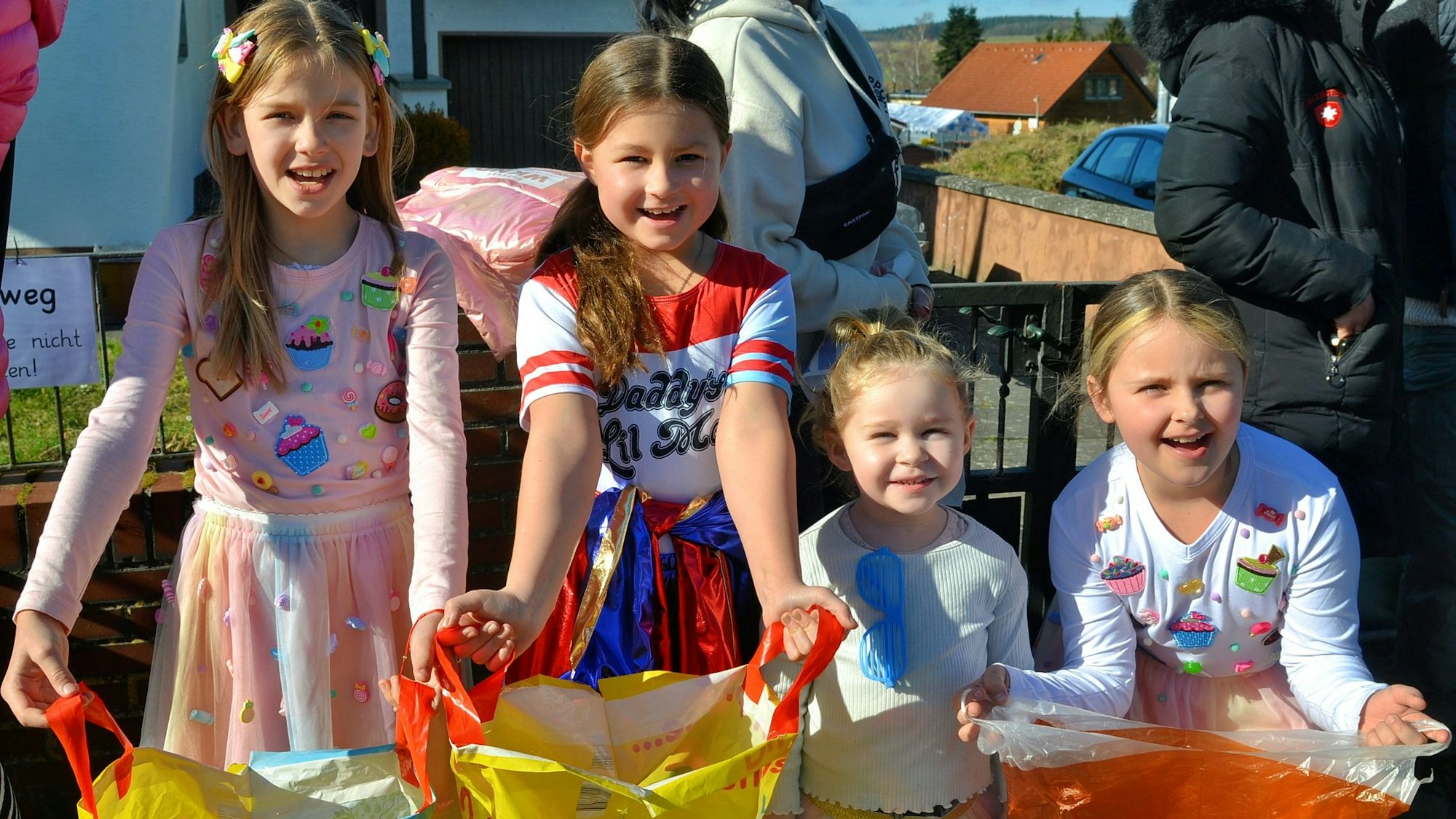 Vier kostümierte Mädchen stehen nebeneinander und breiten ihre Plastiktüten aus.