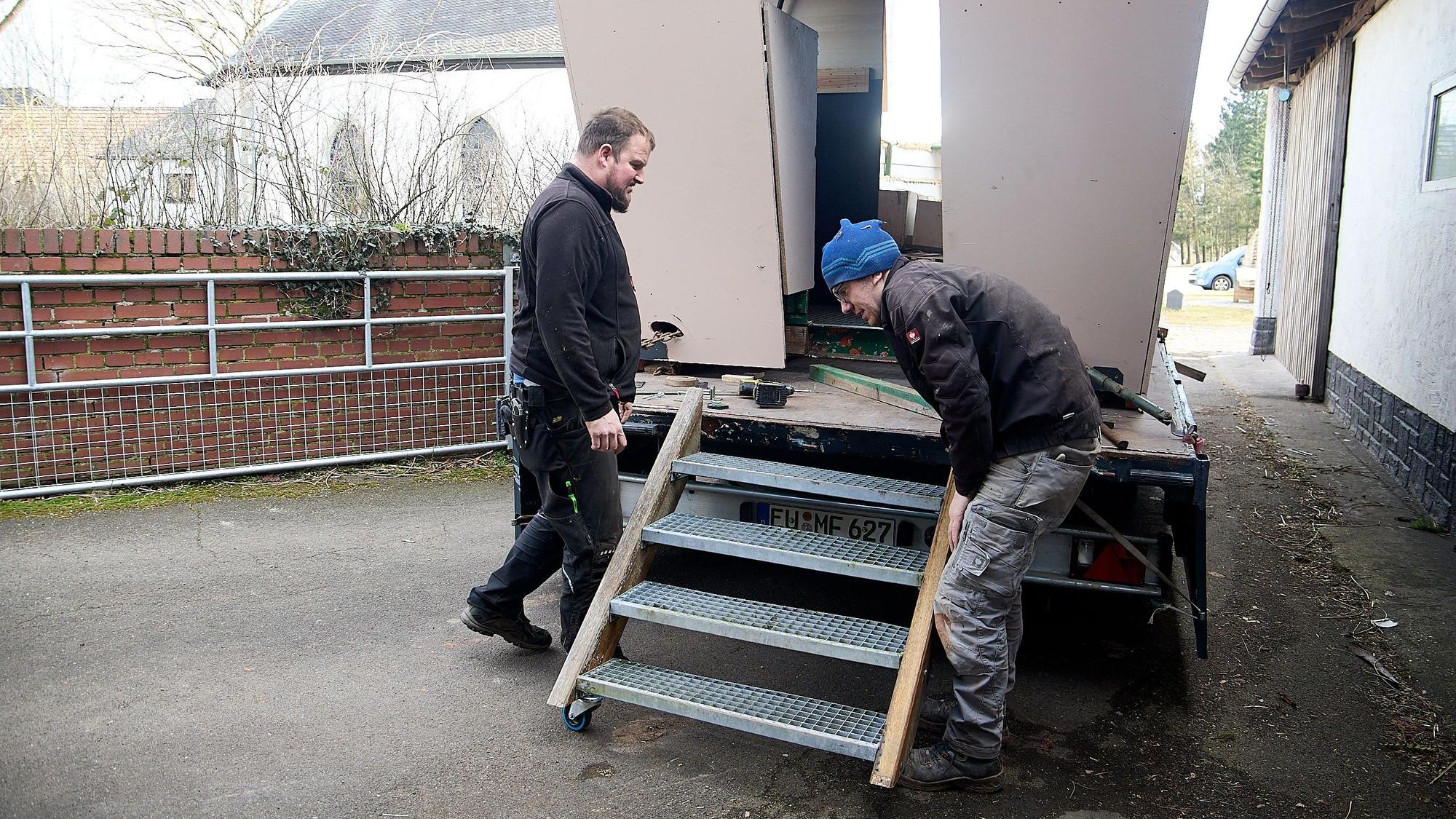 Zwei Männer stehen an einem Karnevalswagen und montieren eine Treppe.