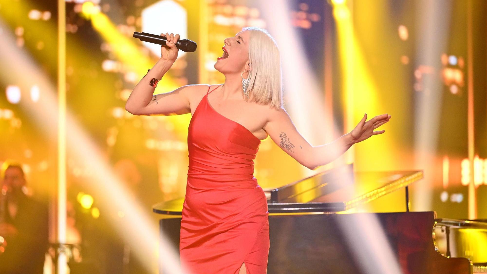 Sängerin Leonora singt im roten Kleid auf der Vorentscheid-Bühne vor einem Flügel.