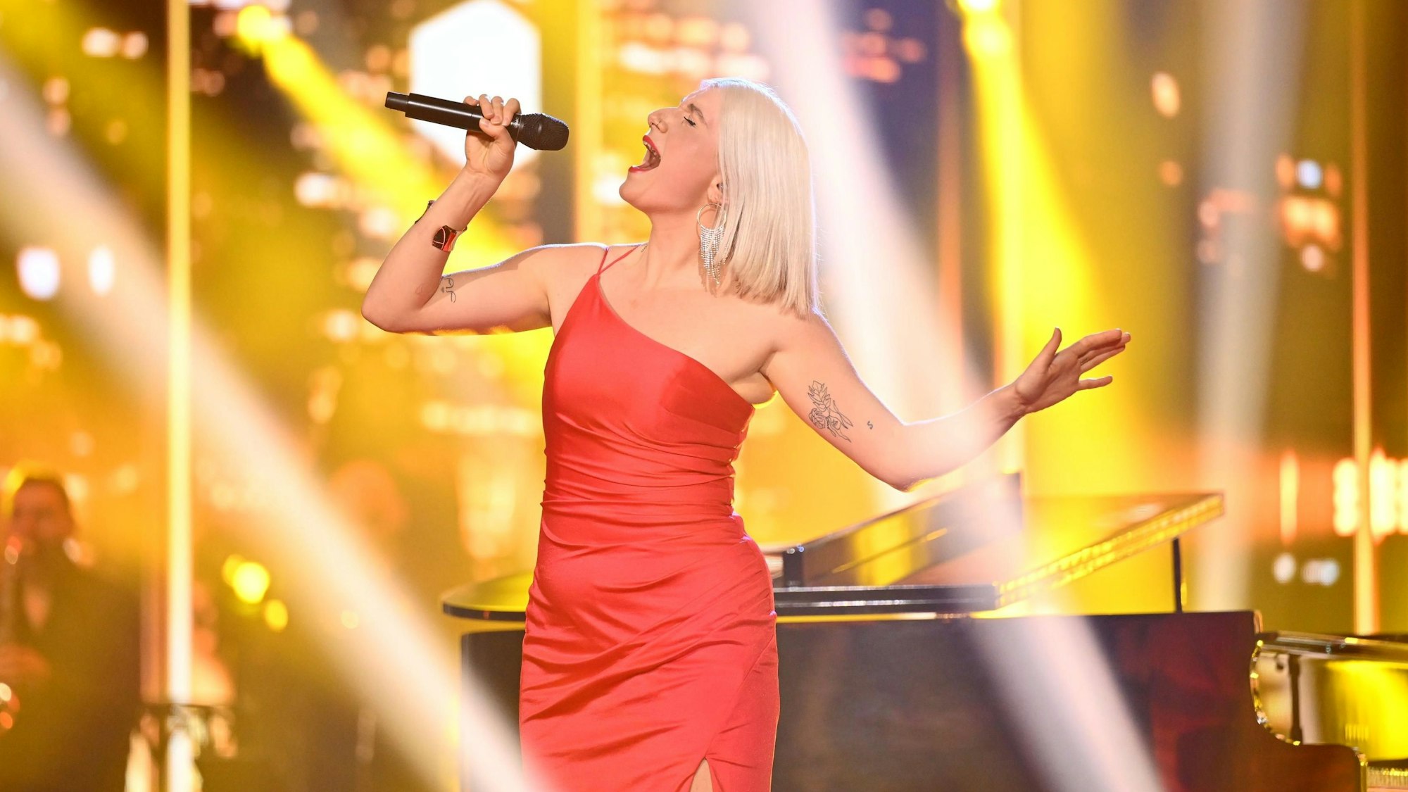 Sängerin Leonora singt im roten Kleid auf der Vorentscheid-Bühne vor einem Flügel.