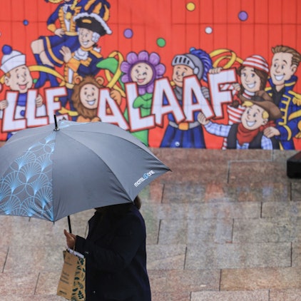 Eine Frau geht mit Regenschirm an einer Tribüne für die Karnevalsumzüge durch die Innenstadt.