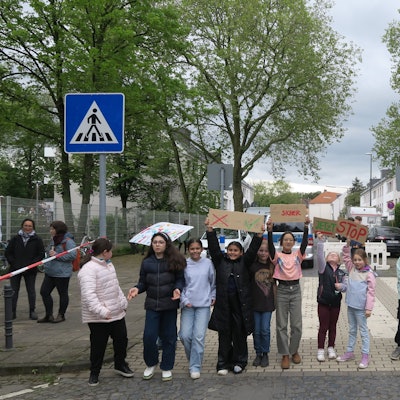 Mehrere Kinder stehen in einer Reihe und blockieren so eine Straße. Sie halten Plakate hoch, auf denen sie einen sicheren Schulweg fordern.
